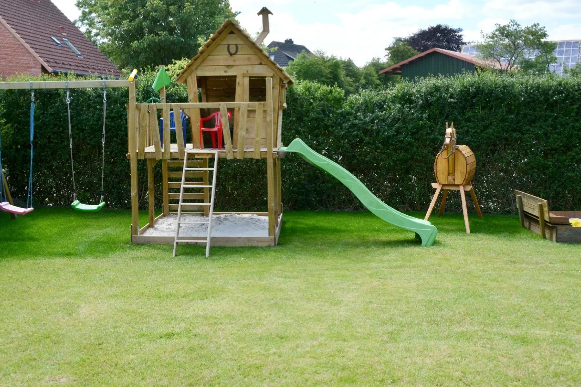 Ein Spielplatz im Garten mit Schaukel und Rutsche.